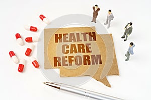 On a white surface are pills, a pen, figurines of people, a sign with the inscription - HEALTH CARE REFORM