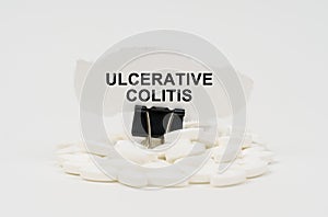 On a white surface are pills and torn paper with the inscription - ULCERATIVE COLITIS