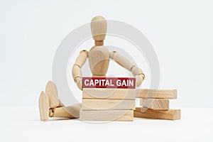 On a white surface sits a wooden man in his hands a block with the inscription - capital gain