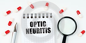 On a white surface are tablets, a pen, a magnifying glass and a notepad with the inscription - Optic neuritis