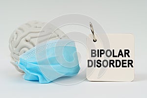On a white surface there is a brain with a blue mask and a notepad with the inscription - Bipolar disorder