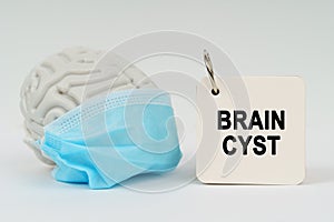 On a white surface there is a brain with a blue mask and a notepad with the inscription - Brain Cyst