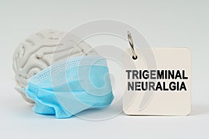 On a white surface there is a brain with a blue mask and a notepad with the inscription - Trigeminal neuralgia