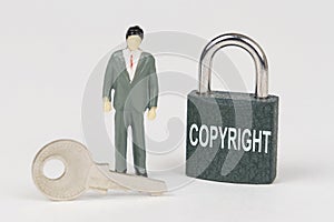 On a white surface there is a figurine of a businessman, a key and a lock with the inscription - COPYRIGHT