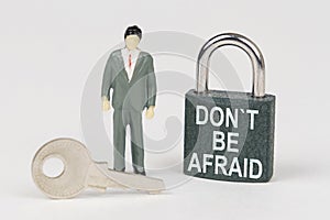 On a white surface there is a figurine of a businessman, a key and a lock with the inscription - Do not Be Afraid