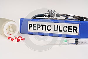 On a white surface there are pills, a syringe and a folder with the inscription - Peptic ulcer