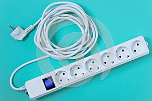 White surge protector with six sockets and  long wire. Turquoise background