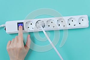White surge protector with sockets.  hand presses the power button. Turquoise background