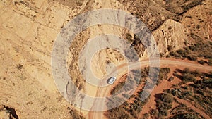 White SUV car driving alone, travel on empty dirt road freeway through desert volcanic landscape at summer sunny day