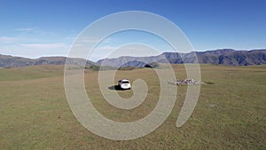 A white SUV drives through mountain green fields