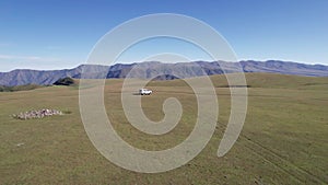 A white SUV drives through mountain green fields