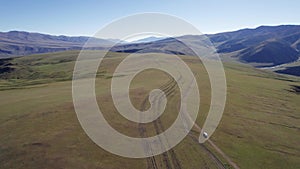 A white SUV drives through mountain green fields