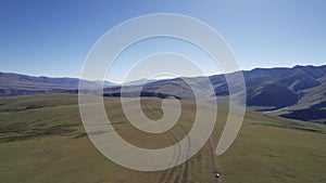 A white SUV drives through mountain green fields