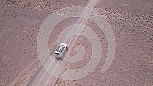 A white SUV is driving fast on a dusty road. Drone