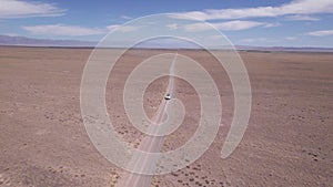 A white SUV is driving fast on a dusty road. Drone