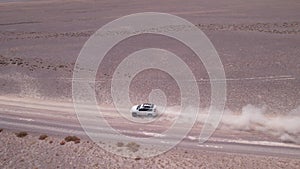A white SUV is driving fast on a dusty road. Drone