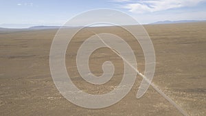 A white SUV is driving fast on a dusty road. Drone