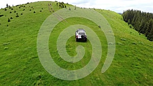 White SUV rides on a mountainous terrain on a dirt road. Aerial view.