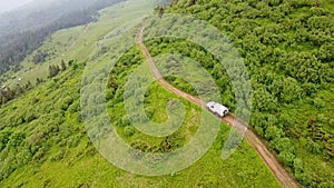 White SUV rides on a mountainous terrain on a dirt road. Aerial view.