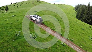 White SUV rides on a mountainous terrain on a dirt road. Aerial view.