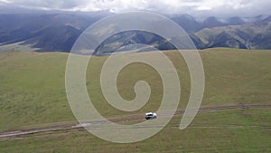 A white SUV rides in the mountains through fields