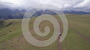 A white SUV rides in the mountains through fields