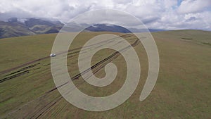 A white SUV rides in the mountains through fields