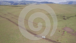 A white SUV rides in the mountains through fields