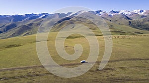 A white SUV rides in the mountains through fields