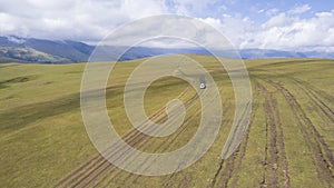 A white SUV rides in the mountains through fields