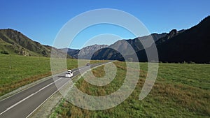 White SUV van riding on traffic asphalt road surrounded picturesque summer mountain
