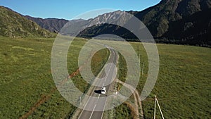 White SUV van roof box riding on asphalt road surrounded summer mountain