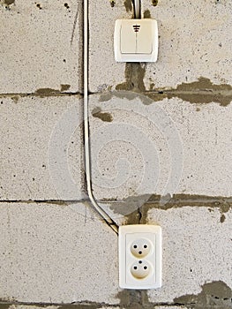 White switch and white socket on a brick wall.