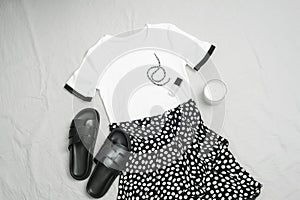 White T-shirt, black skirt, sandals and accessories on grey background. Overhead view of woman's casual day outfit