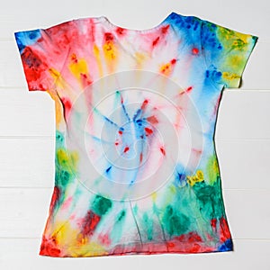 White t-shirt hand painted in tie dye style on white table.