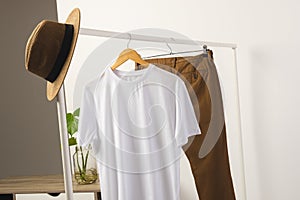 White t shirt, hat and brown trousers hanging from clothes rail with copy space on white background