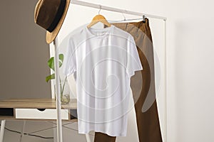 White t shirt, hat and brown trousers hanging from clothes rail with copy space on white background