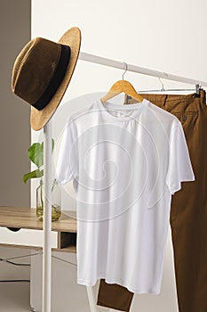 White t shirt, hat and brown trousers hanging from clothes rail with copy space on white background