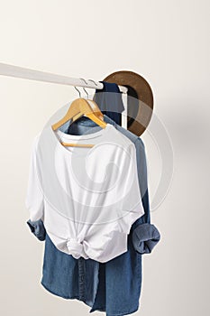 White t shirt, hat and denim shirt hanging from clothes rail with copy space on white background