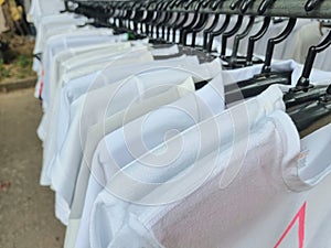 A white t-shirt is hung on a rail for customers to come in and buy. In a market in Thailand