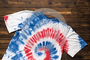 White T-shirt painted in blue and red in tie dye style on a wooden table. The concept of self-dyeing clothes