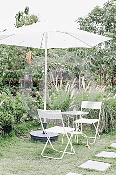 White Table,chair set and patio umbrella for relaxing with nature atmosphere in the outdoor garden the tree shade with the afterno