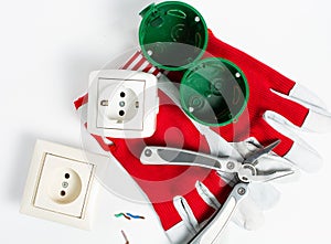 on a white table  a disassembled electrical outlet  ready to install  stripped wires and a red screwdriver with protective gloves