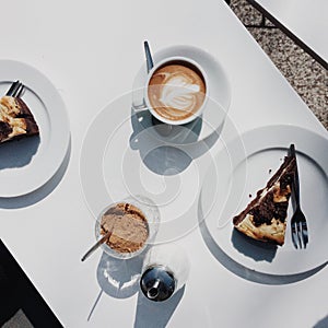 White table with great coffee latte and chocolate cake in the sun