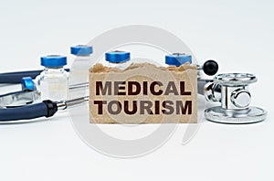 On a white table lie ampoules, a stethoscope and a cardboard with the inscription - MEDICAL TOURISM
