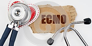 On a white table lie a heart, a stethoscope and a cardboard with the inscription - ECMO