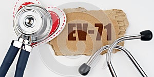 On a white table lie a heart, a stethoscope and a cardboard with the inscription - EV-71