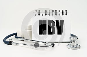 On a white table lies a stethoscope, pills and a notebook with the inscription - HBV
