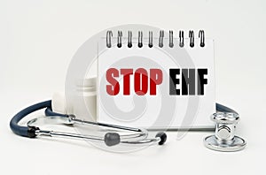 On a white table lies a stethoscope, pills and a notebook with the inscription - Stop EHF