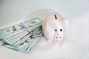 On the white table near hundred-dollar bills is a pink piggy Bank